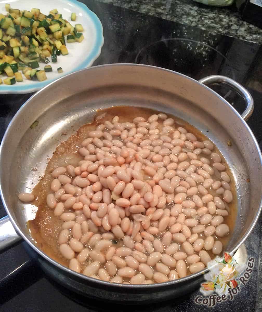 Smash or chop the garlic cloves and put them in the pan, pouring the beans with liquid over the garlic. Cook for about ten minutes over medium heat, stirring frequently. If the beans start to get dry, add some stock, white wine or water. 
