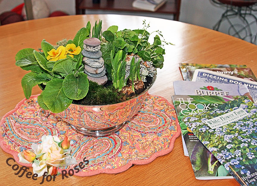Add bits of lichen, moss or other natural materials to the bare areas, and place your rocks in the garden. One of the nice things about a silver Revere bowl is that it reflects what is underneath it, so use a spring-like place mat to your advantage. Then grab some plant and seed catalogs and think spring.
