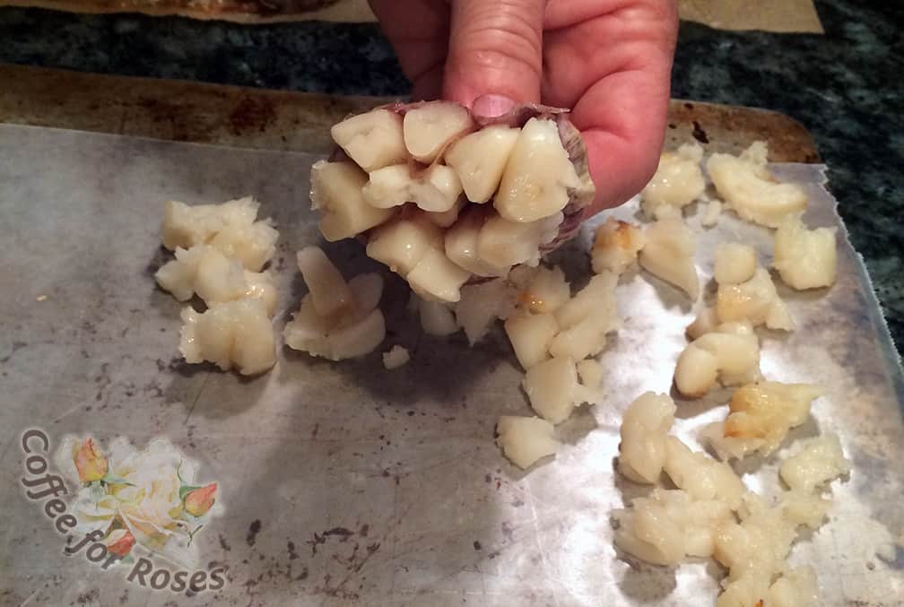 Once the garlic is done remove it from the oven and let it cool enough so you can comfortably handle it. Pick the heads up one by one and squeeze the cloves out of the paper onto a waxed paper covered cookie sheet. 