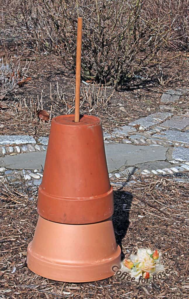 Put one of the widest pots upside down on the ground to form a sturdy base. Find another pot that fits on top of that one, be it bottom-to-bottom or both upside down as you see here. Stick the dowel or other rod through the holes and into the ground to stabilize the stack.